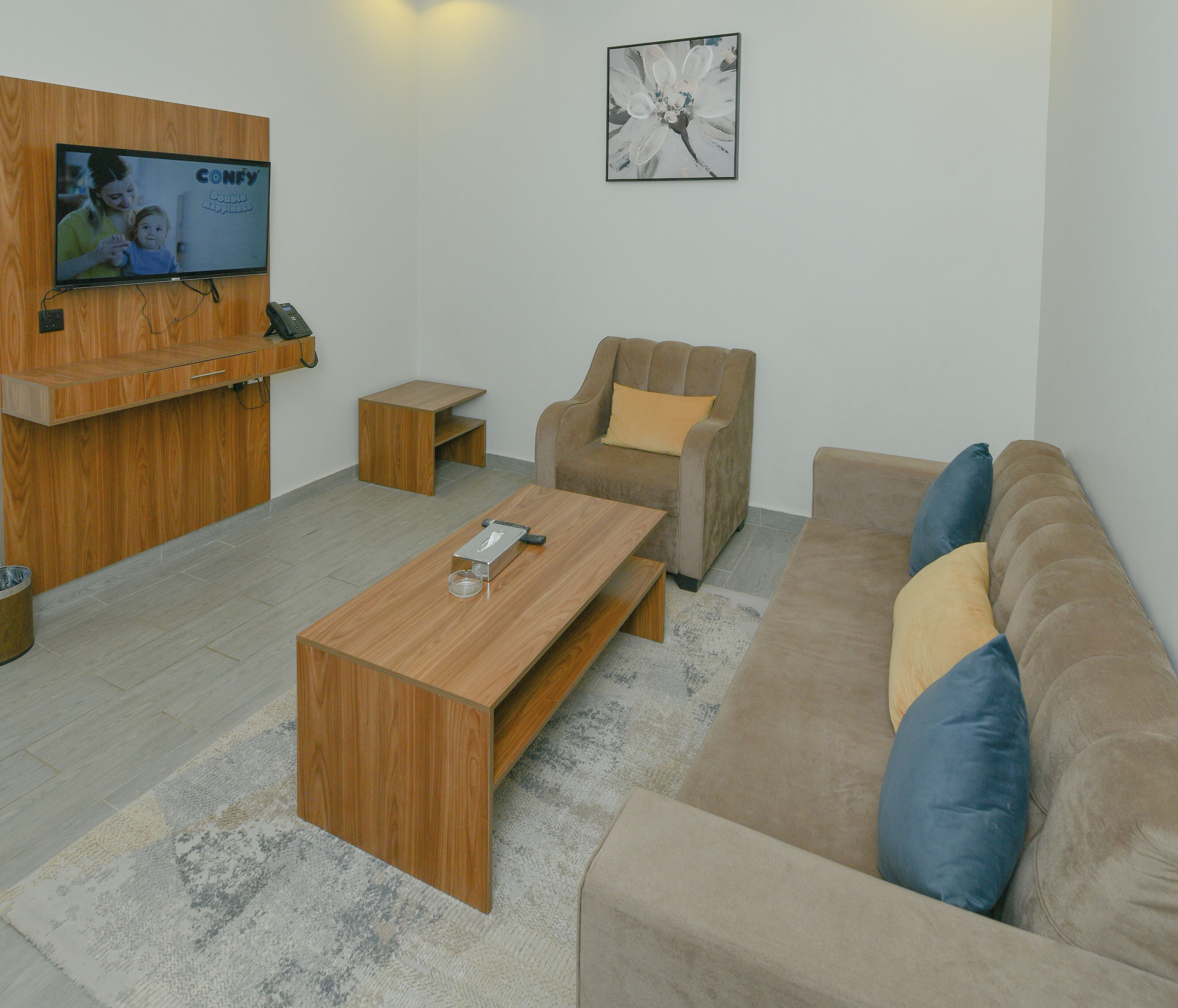 Uma sala de estar moderna com uma mesa de centro de madeira, sofá bege e uma televisão fixada em uma parede de madeira.
