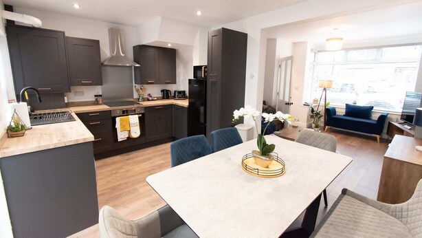 Une cuisine moderne avec des meubles de couleur sombre, un îlot central et un coin repas comprenant une table et des chaises.