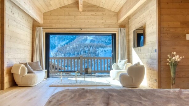 A log cabin interior with a large window, a balcony, and a cozy seating area.