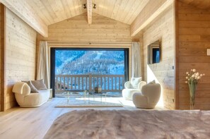 L’intérieur d’une cabane en rondins, avec une grande fenêtre, un balcon et un coin salon confortable.