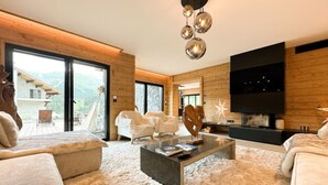 A modern living room with a large TV, a fireplace, and a view of a mountain.