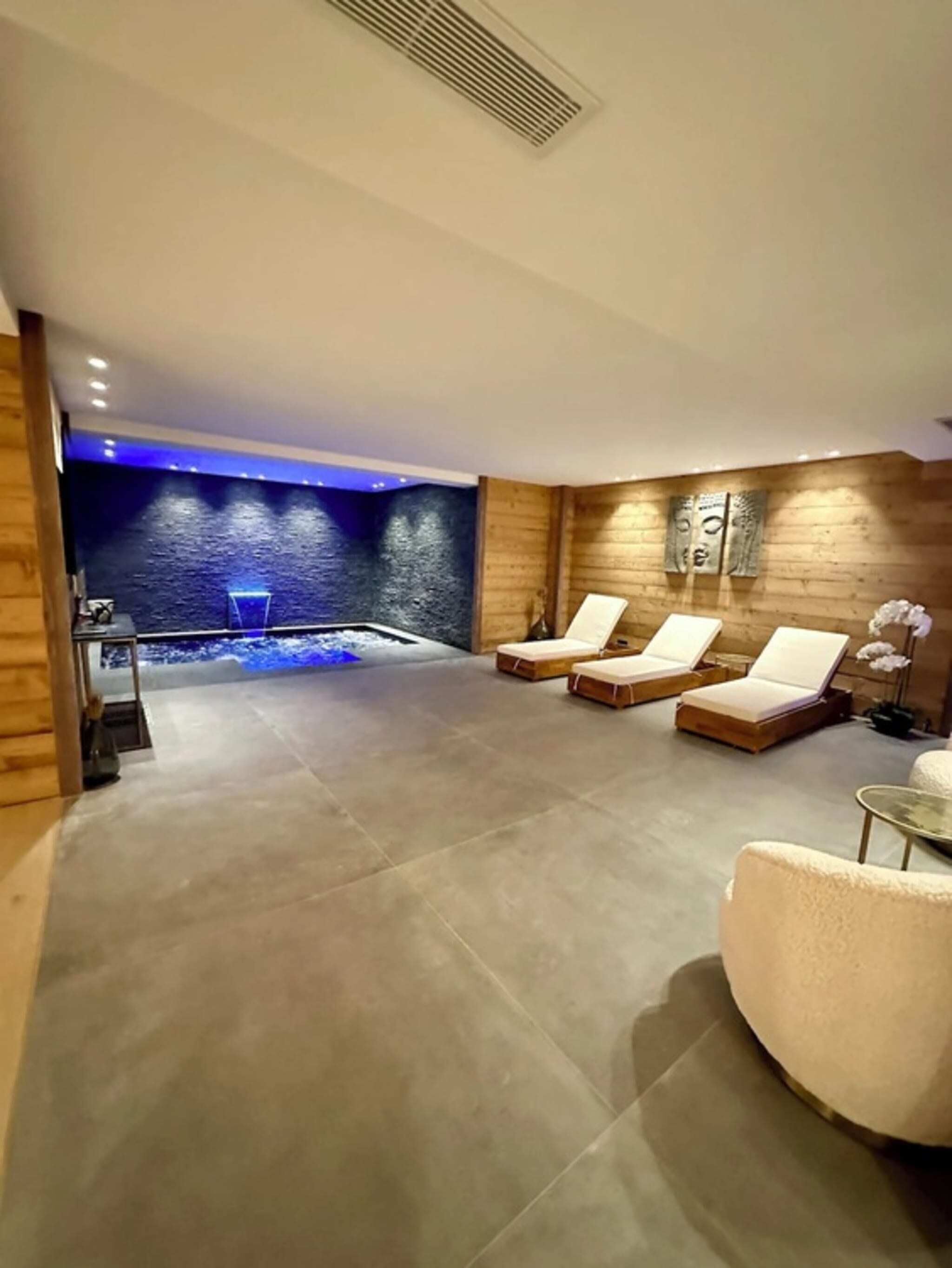 A spa area with a stone wall, a water feature, and three lounge chairs.