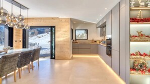 A modern kitchen with a wooden accent wall, a dining area with a view of a snowy landscape, and holiday decorations on shelves.