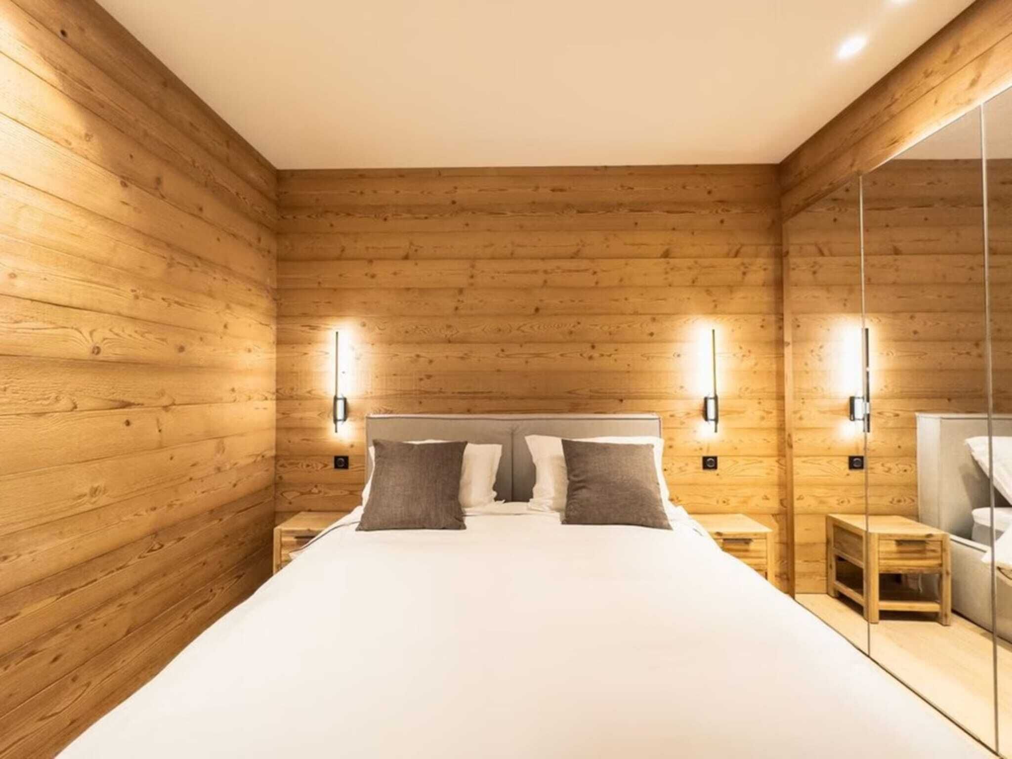 A room with wooden walls, a bed with white bedding, two bedside tables, and wall-mounted lights.