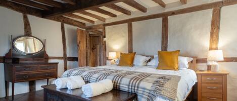 A bedroom with a wooden ceiling, a large bed with plaid bedding, two bedside tables with lamps, a wooden dresser, and a mirror.
