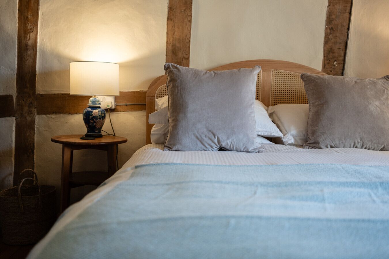 Cama bem arrumada com colcha listrada, cabeceira de madeira e abajur sobre uma pequena mesa de cabeceira de madeira.