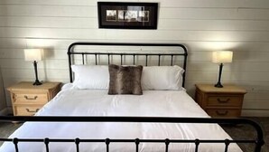 Una cama con ropa blanca, cabecera de metal negro y dos mesitas de noche con lámparas.