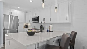 A modern kitchen with white cabinetry, stainless steel appliances, and a central island with seating.