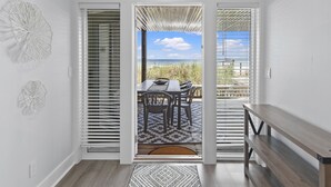 A room with a view of the beach through a sliding glass door, a wooden bench, and a patterned rug.
