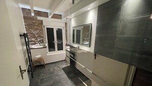A modern bathroom with a stone accent wall, a glass shower enclosure, and a large mirror. - Luxury Apartment Atypical (Épinal)