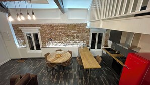 A modern kitchen with a stone wall backsplash, a wooden dining table with chairs, a red refrigerator, and a built-in oven. - Luxury Apartment Atypical (Épinal)