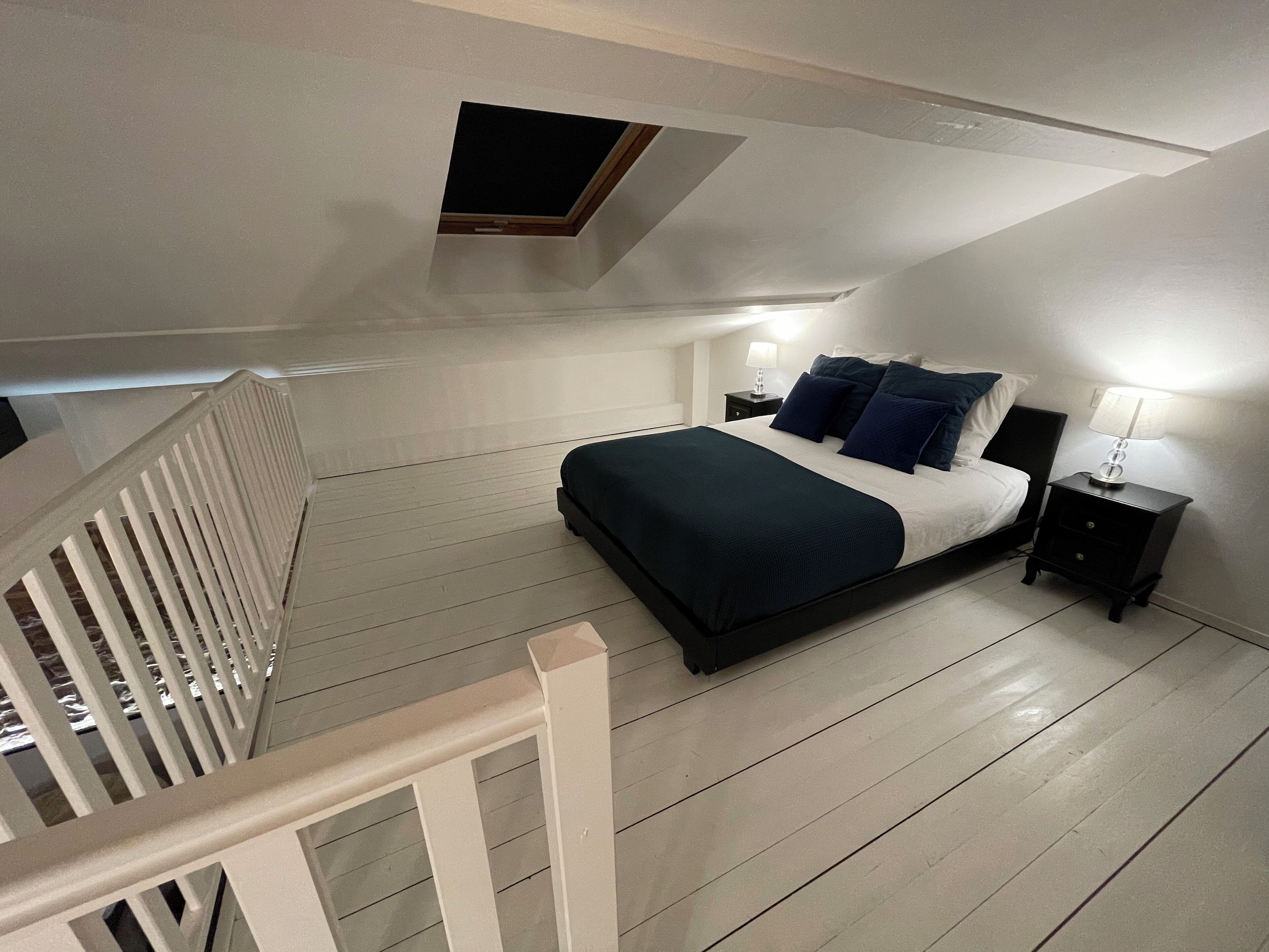 Un dormitorio con cama, mesitas de noche, una ventana y barandilla blanca.
