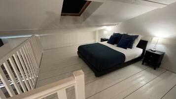 Un dormitorio con cama, mesitas de noche, una ventana y barandilla blanca.