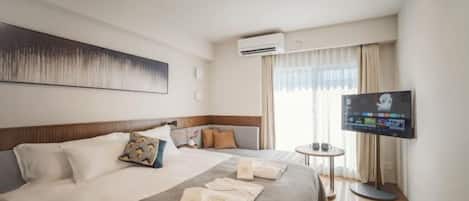 A hotel room with a large bed, a flat-screen TV, a small round table, and a window with curtains.