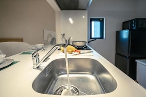 A modern kitchen with a stainless steel sink, a faucet, a bowl, and a refrigerator.