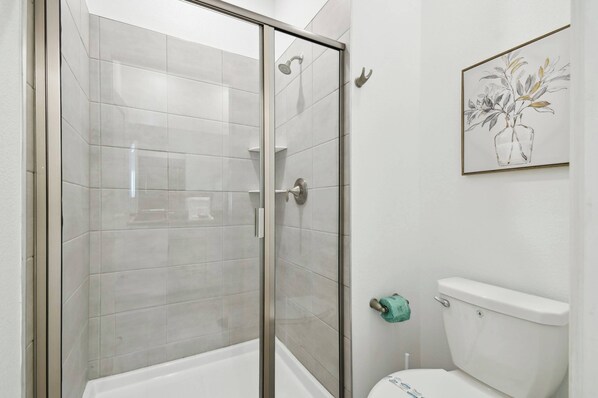 A modern bathroom with a glass-enclosed shower, a toilet, and a framed artwork on the wall.