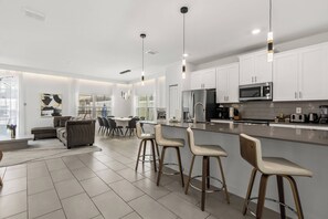 A modern kitchen with white cabinets, stainless steel appliances, and a bar area with stools. - 5BR to Gather, Relax and Make Memories (2640ST) (Kissimmee)