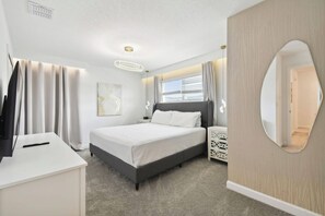 Une chambre d’hôtel moderne équipée d’un lit, d’un bureau, d’une télévision et d’un grand miroir.