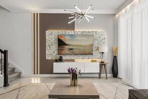 A modern living room with a marble fireplace, a large painting, a console table, and a minimalist chandelier.