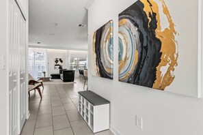 A modern interior with a hallway leading to a dining area, featuring a bench and abstract wall art. - 5BR to Gather, Relax and Make Memories (2640ST) (Kissimmee)