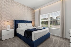 A bedroom with a large bed, a nightstand, a lamp, and a window with blinds.