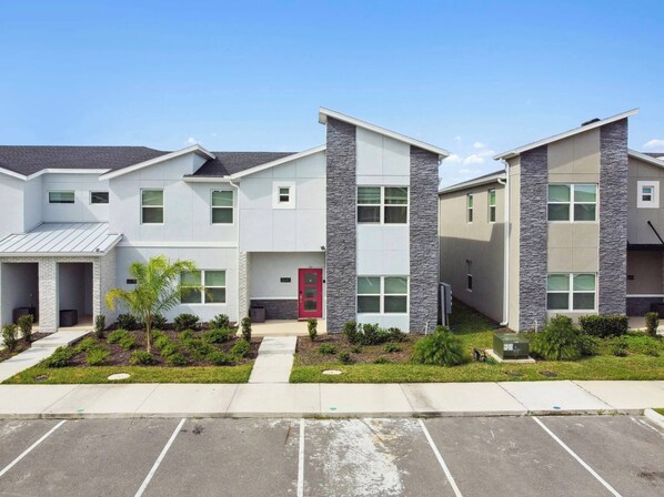 Un immeuble moderne à plusieurs étages, dont la façade est un mélange de pierre et de stuc, avec une porte rouge et un parking situé à l’avant.