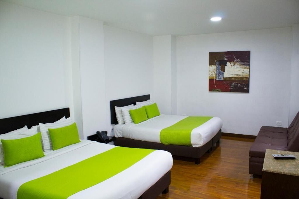 A hotel room with two beds, a couch, a painting on the wall, and a remote control on the table.