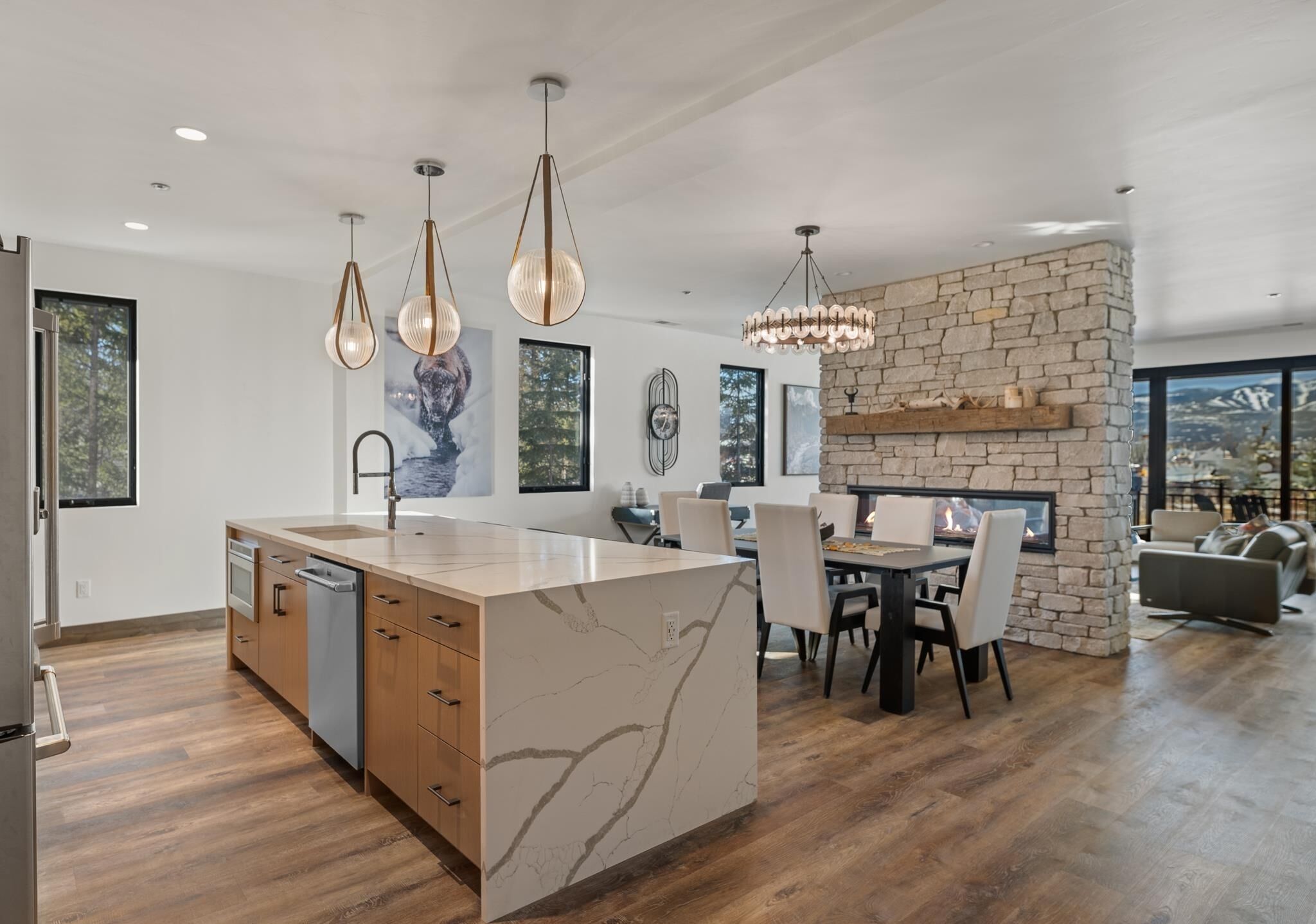 A modern kitchen with a marble island, pendant lights, and a stone fireplace.
