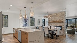 A modern kitchen with a marble island, pendant lights, and a stone fireplace.