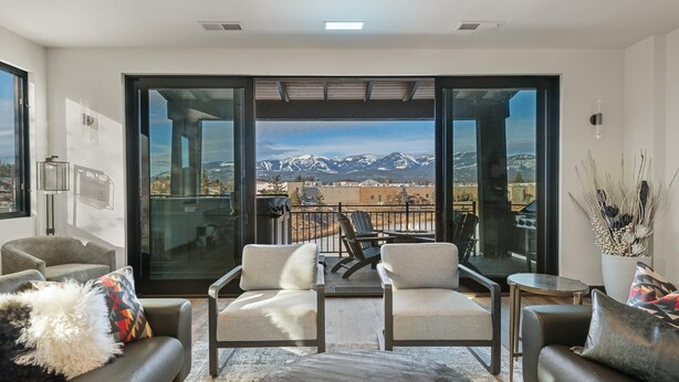 A modern living room with a balcony, large windows, and a view of snow-capped mountains.