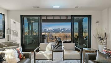A modern living room with a balcony, large windows, and a view of snow-capped mountains.