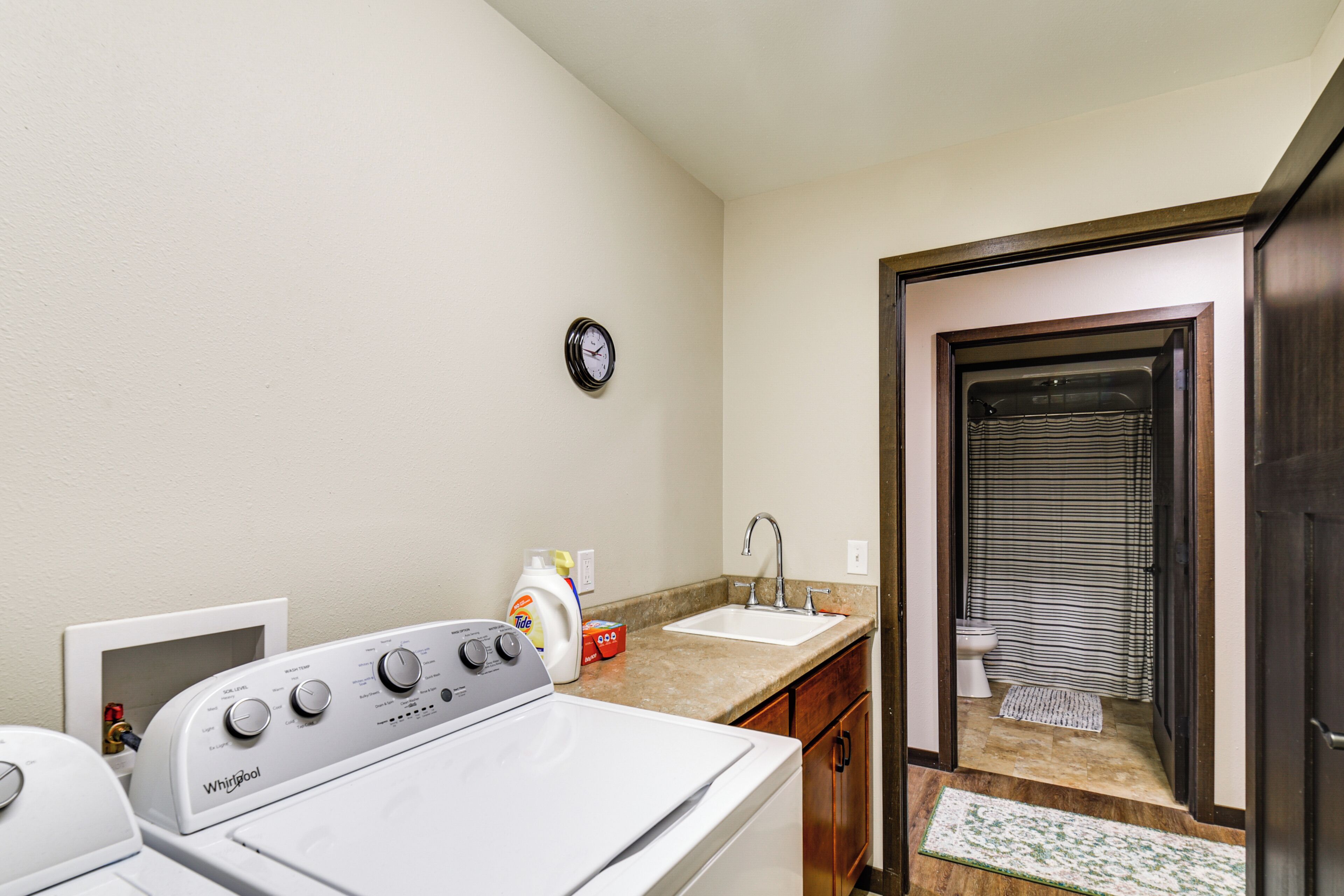 A laundry area with a washer and dryer, a sink, and a clock on the wall.