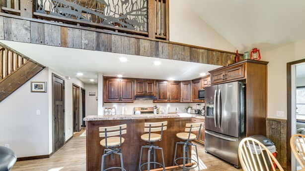 A spacious kitchen with a central island, bar stools, a refrigerator, and a staircase leading to an upper level. - Covered Porch & Grill: 1-Acre Property in Bristow! (Bristow)