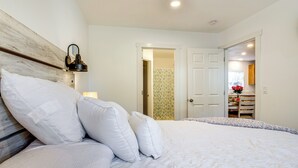 A bedroom with a large bed, white bedding, a wooden headboard, a nightstand with a lamp, and a door leading to a bathroom. - Near Ocean: 'Home Away From Home' in Gold Beach (Gold Beach)