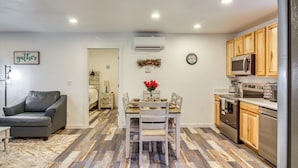 A compact kitchen with wooden cabinets, a dining table with chairs, and a gray leather couch. - Near Ocean: 'Home Away From Home' in Gold Beach (Gold Beach)