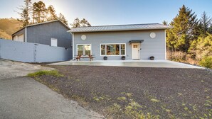 A modern single-story house with a grey exterior, a front porch with a bench, and a small garden area. - Near Ocean: 'Home Away From Home' in Gold Beach (Gold Beach)