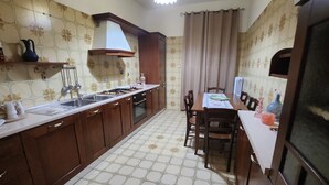 A kitchen with a gas stove, sink, and wooden cabinets. There is a dining table with chairs and a window with curtains. - Cozy apartment a few meters from the Baiano highway exit. (Sirignano)
