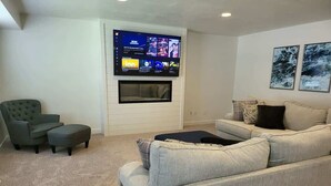 A living room with a grey sofa, a grey armchair, and a TV mounted on the wall. - Close to Marina & Market · 3BR House · Sleeps 10 (Garden City)