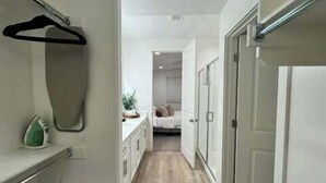 A narrow hallway leading to a bedroom with a bed, a dresser, and a hanging garment rack. - Close to Marina & Market · 3BR House · Sleeps 10 (Garden City)