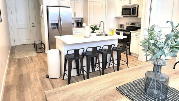 A modern kitchen with white cabinets, a central island with bar stools, stainless steel appliances, and pendant lighting. - Close to Marina & Market · 3BR House · Sleeps 10 (Garden City)