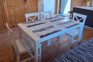 A dining area with a white table and chairs, a bench, and a kitchen in the background.
