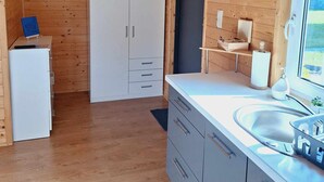 A compact kitchen with wooden walls, a white refrigerator, a sink, and a window. - Holiday Homes Close to the Seaside Beach (Mielno)