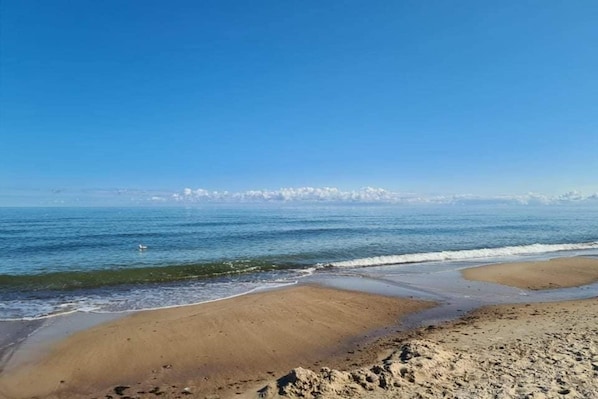 A beach with clear skies, calm water, and distant mountains.