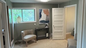 A room with a carpeted floor, a desk with a chair, a door, and a window with a view of greenery. - Cozy 2BD Retreat Near Danceland in Manitou Beach (Manitou Beach)