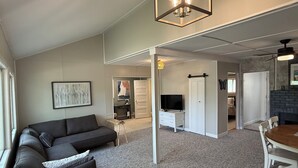 A modern living room with a sofa, coffee table, and a dining area with a table and chairs. There is a TV and a fireplace in the background. - Cozy 2BD Retreat Near Danceland in Manitou Beach (Manitou Beach)