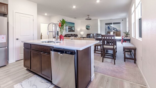 A modern kitchen with a dishwasher, a dining area with a bench, and a living room with a sofa and a TV.
