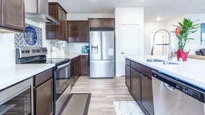 A modern kitchen with stainless steel appliances, wooden cabinets, and a marble countertop.