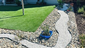 A landscaped backyard with a lawn, a curved gravel path, and potted plants.