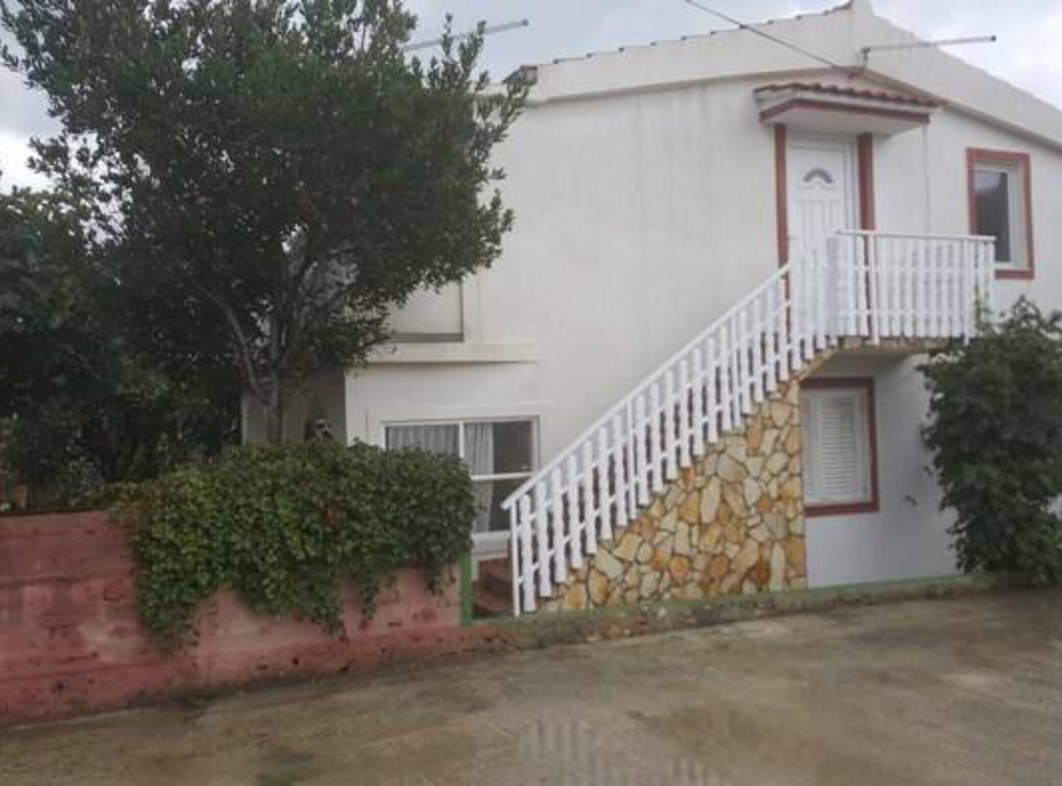A two-story house with a white exterior, a stone staircase, and a small balcony.