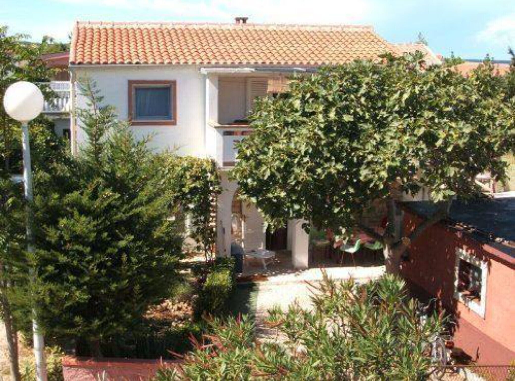 A two-story house with a tiled roof, surrounded by greenery and a small garden.